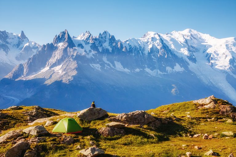 Person sitting on a rock next to a tent overlooking Mont Blanc